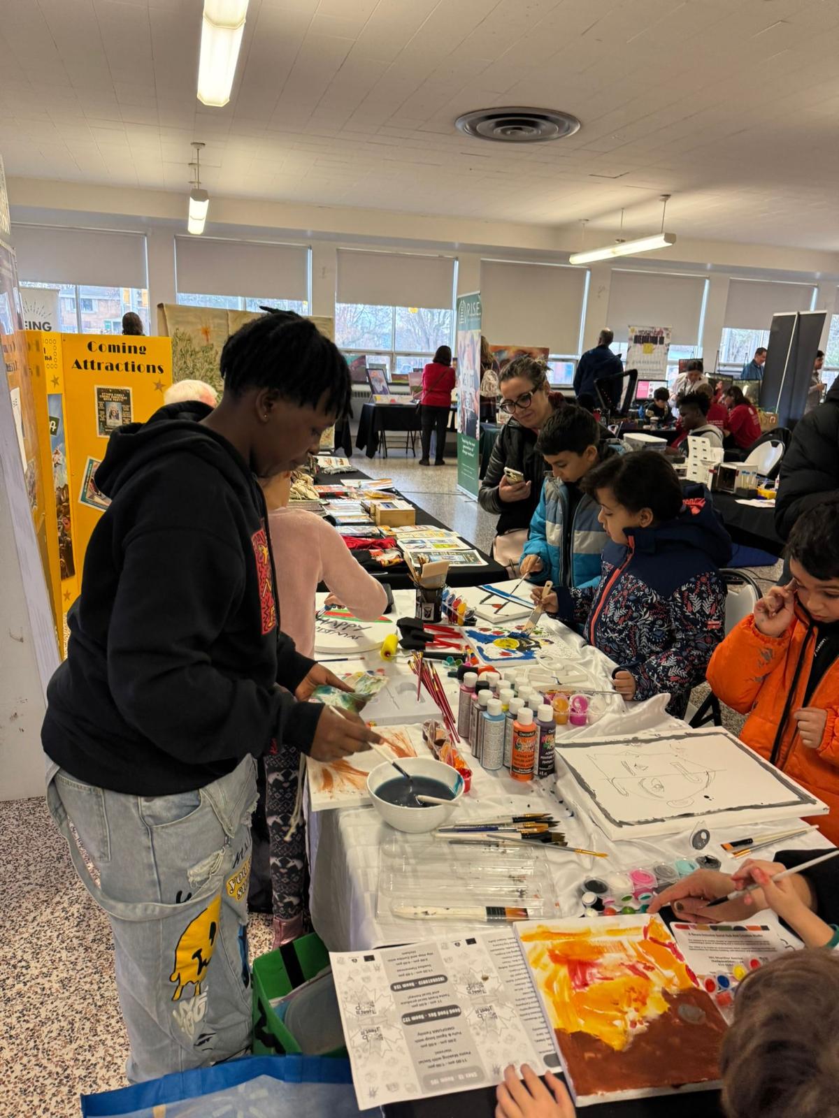 Youth helping children paint at a community art table.